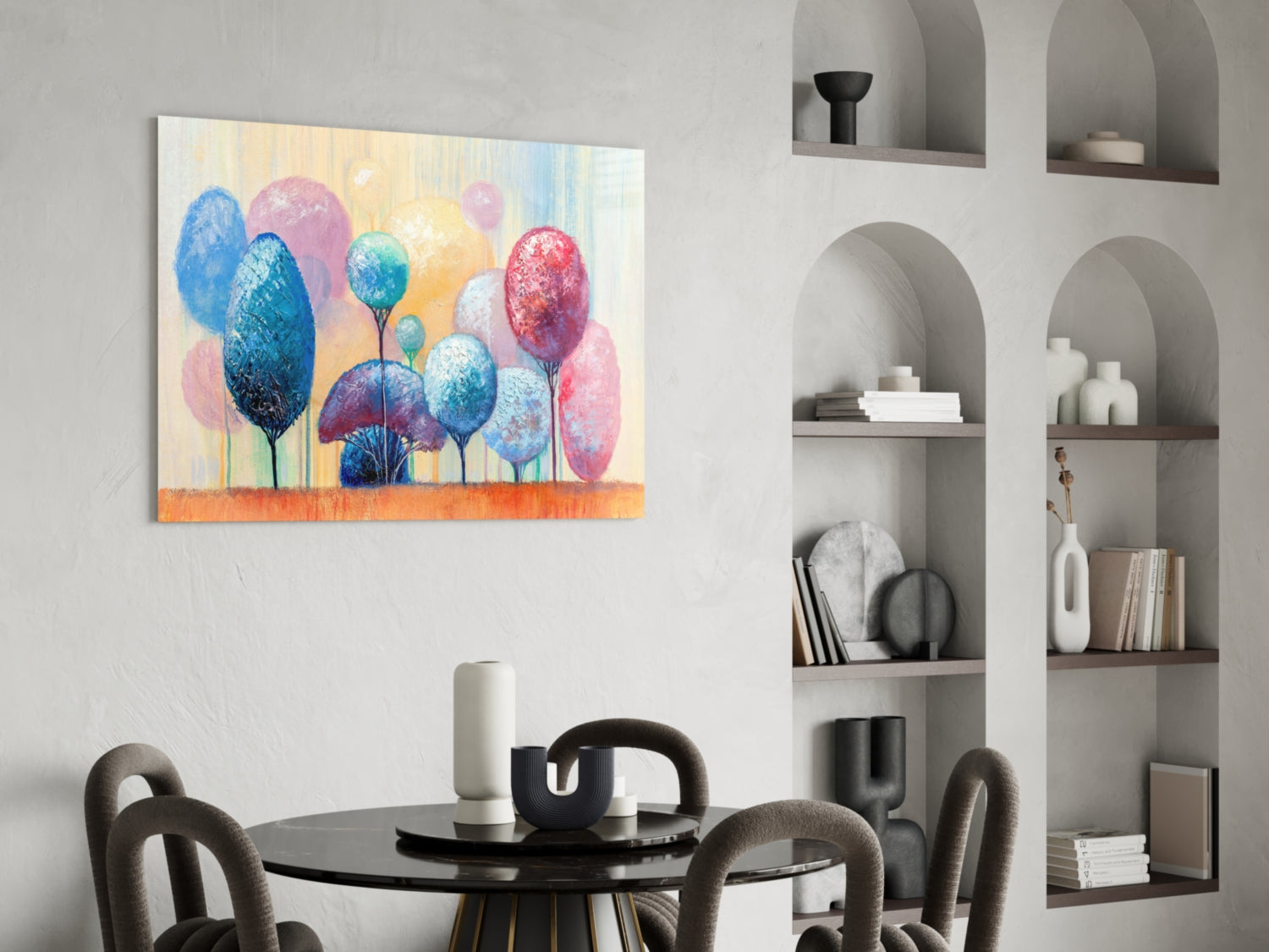 Colorful glass wall art featuring blue, pink, and yellow trees displayed above a black dining table in a modern interior with built-in shelving.