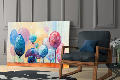 Colorful glass wall art featuring stylized trees with blue, pink, and red foliage displayed in modern interior setting beside wooden chair.