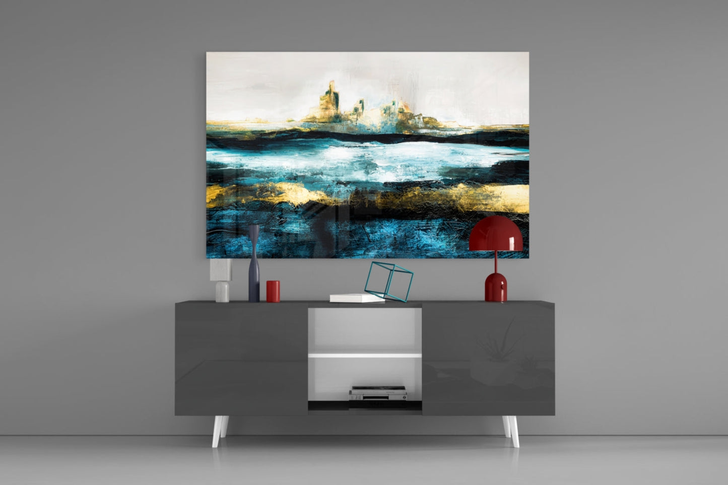 Glass wall art depicting layered seascape with turquoise water and gold accents mounted above gray media console with red lamp and accessories.