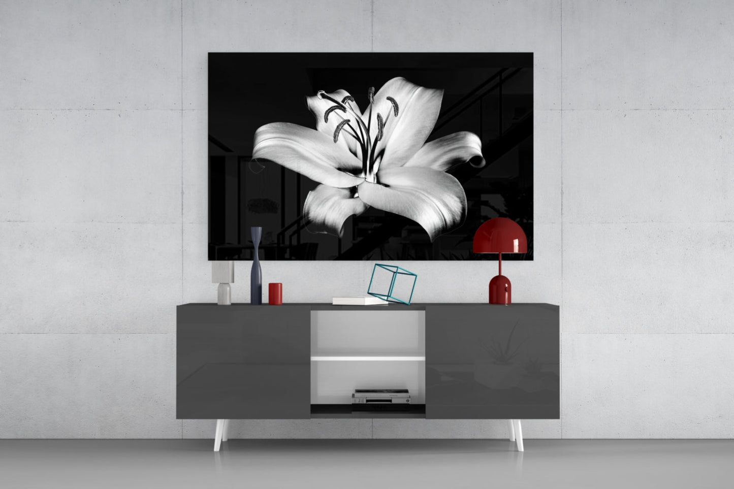 Black and white lily flower glass wall art displayed above gray media console with red lamp and decorative accessories.