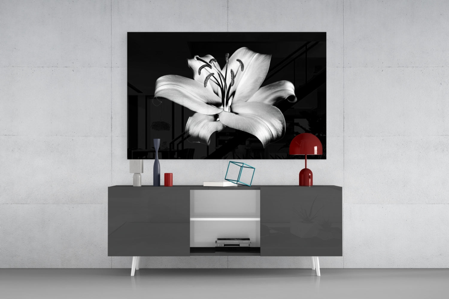 Black and white lily flower glass wall art displayed above gray media console with red lamp and decorative accessories.