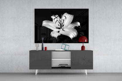 Black and white lily flower glass wall art displayed above gray media console with red lamp and decorative accessories.