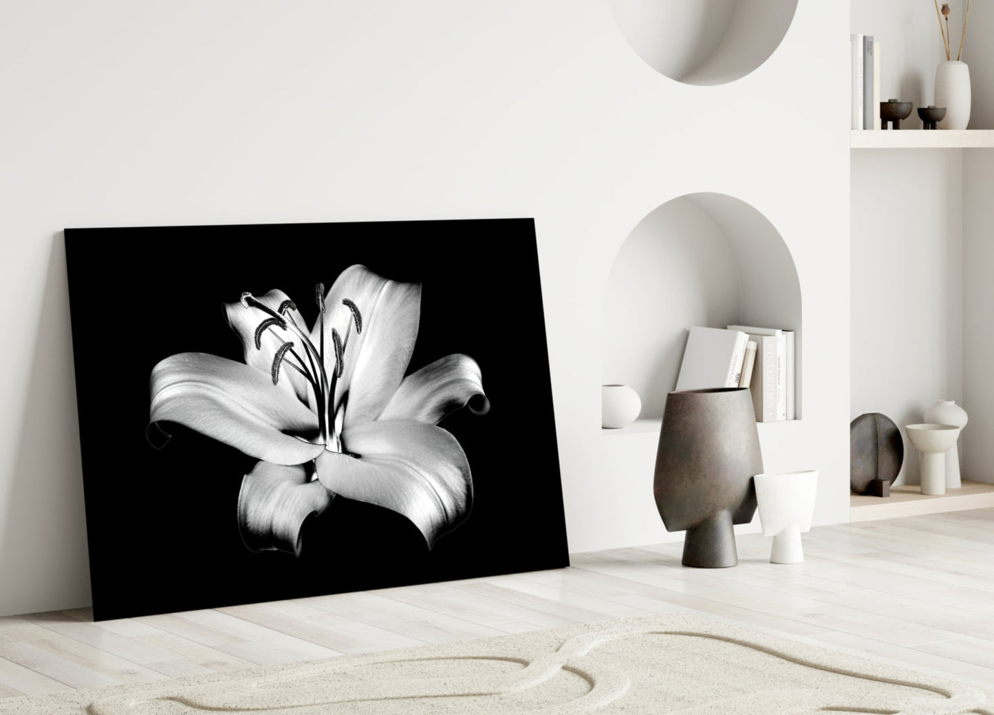 Black and white lily glass wall art leaning against white wall in minimalist interior setting with decorative objects.