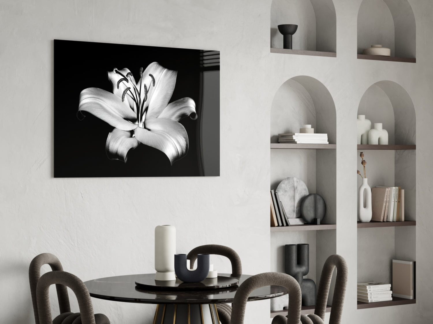 Black and white lily flower glass wall art displayed above a round black dining table with curved chairs and shelving unit.