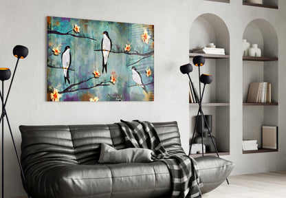 Glass wall art depicting stylized birds perched on branches with yellow flowers against textured turquoise and purple background, displayed above black leather sofa.