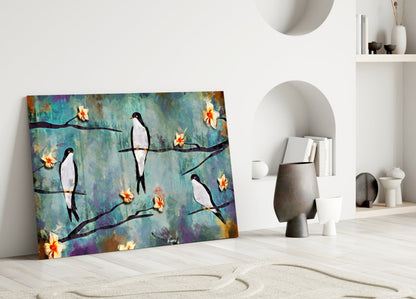 Colorful glass wall art leaning against white wall displays stylized black birds perched on branches with yellow flowers against textured teal and purple background.