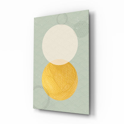 A glass wall art panel displaying a cream circle above a yellow oval on a seafoam green patterned background, viewed at an angle.