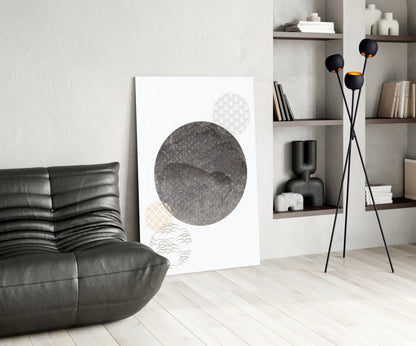Black Moon Glass Wall Art leaning against white wall in minimalist living room with leather sofa and shelving.