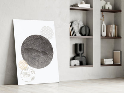 Modern minimalist interior with black moon glass wall art leaning against wall beside built-in shelving displaying books and ceramic decorative objects.