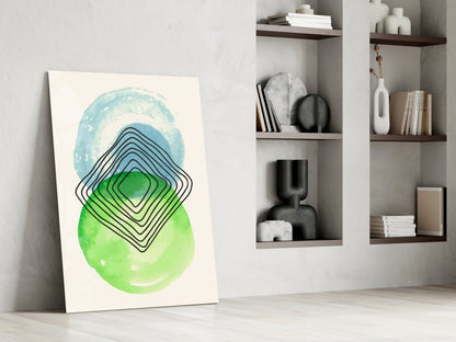 Abstract glass wall art leaning against white wall displaying blue, green, and black concentric geometric shapes with watercolor circles.
