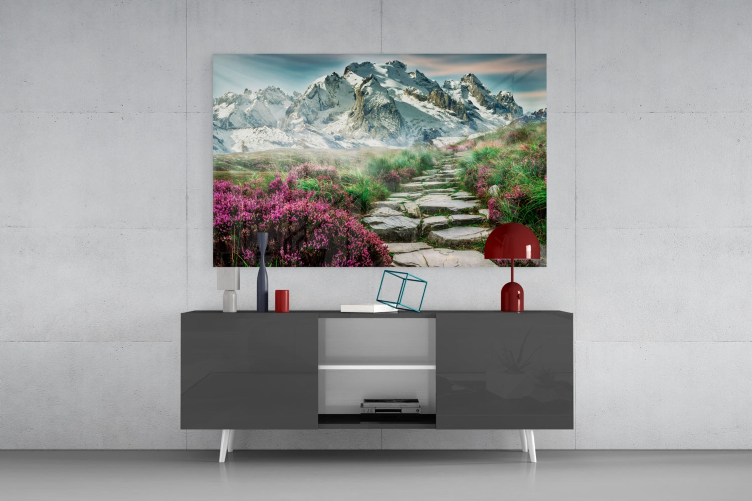 Glass wall art depicting a mountain landscape with purple flowers and stone pathway displayed above a dark media console in a modern living room setting.
