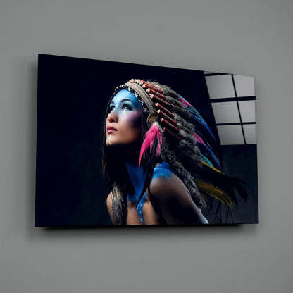 Glass wall art panel displaying woman with blue face paint and colorful feathered headdress against dark background, mounted on gray wall.