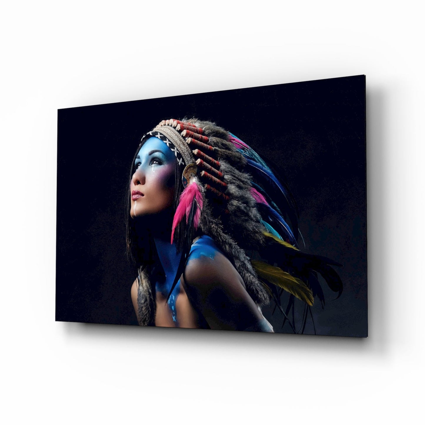 Woman with blue face paint and colorful feathered headdress against black background on glass wall art panel.