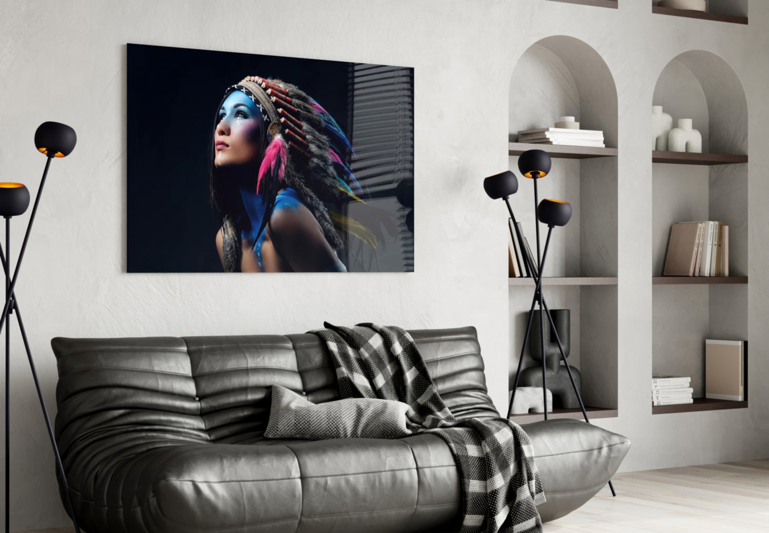 Glass wall art featuring a woman with blue face paint and colorful feathered headdress displayed above a gray sofa in modern interior setting.