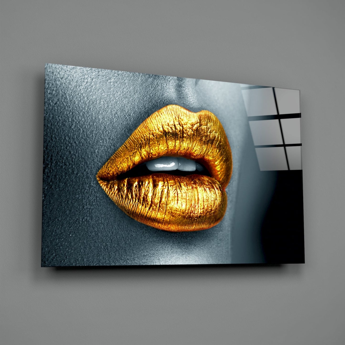 Golden metallic lips on gray textured background displayed as angled glass wall art panel with color reference grid.