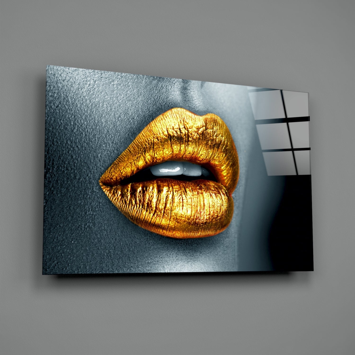 Golden metallic lips on gray textured background displayed as angled glass wall art panel with color reference grid.