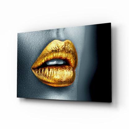 Angled perspective view of a glass wall art panel featuring golden metallic lips against a dark blue-grey textured background.