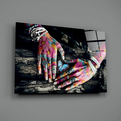 Colorful tattooed hands resting on dark wood, displayed as a glass wall art print with vibrant pink, blue, and yellow hues.