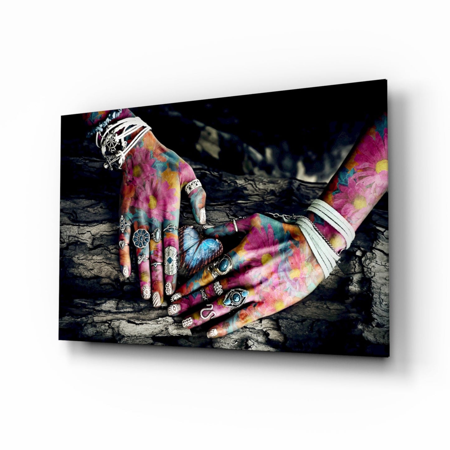 Colorful tattooed hands with rings and white wraps resting on cracked dark ground, displayed as framed glass wall art.
