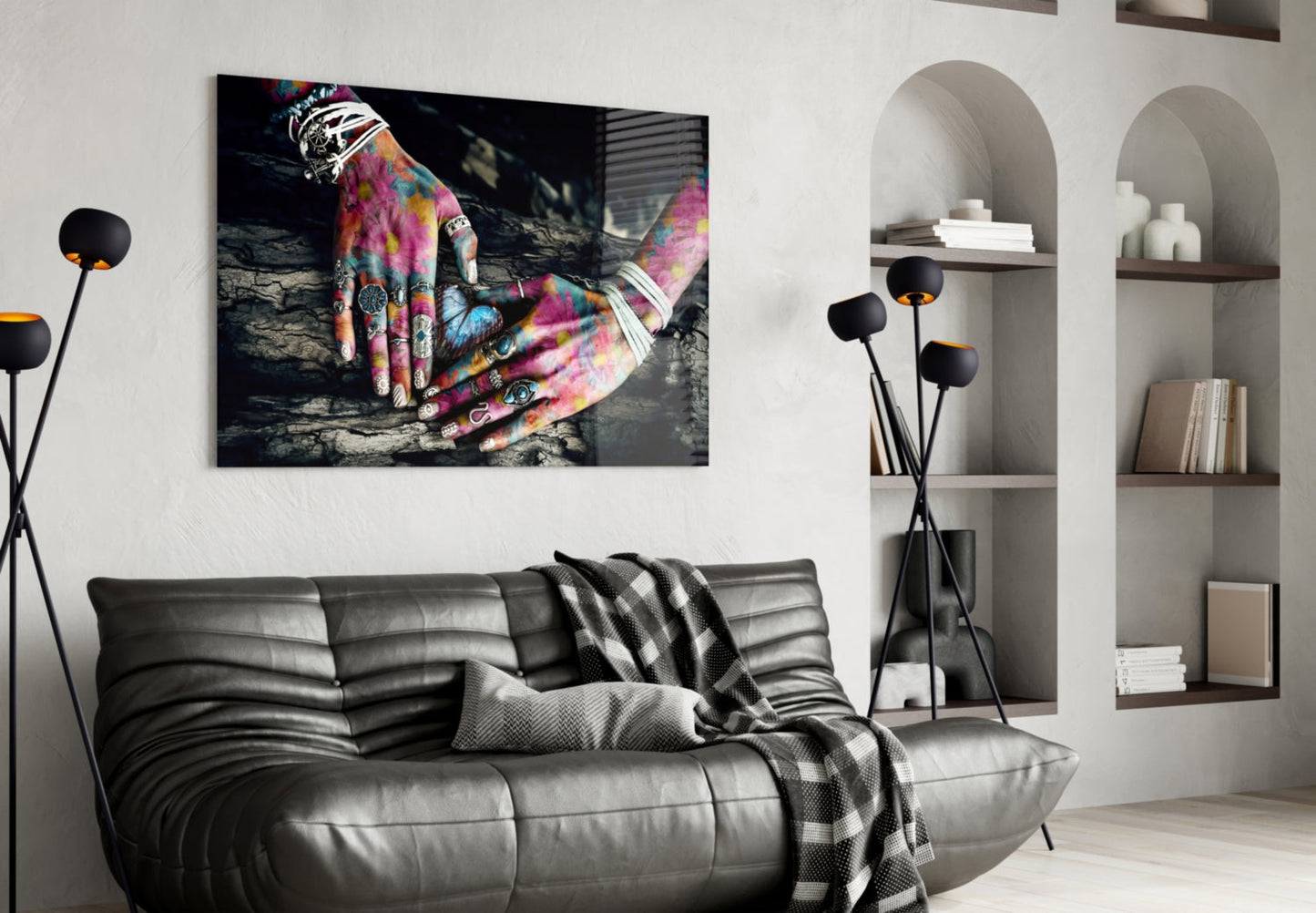 Colorful tattooed hands displayed on glass wall art above a grey leather sofa in a modern living room setting.