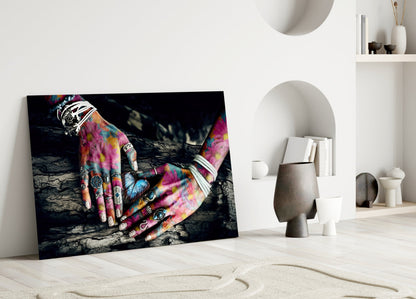 Vibrant glass wall art displaying colorful tattooed hands leaning against textured dark background, displayed in minimalist white interior setting.
