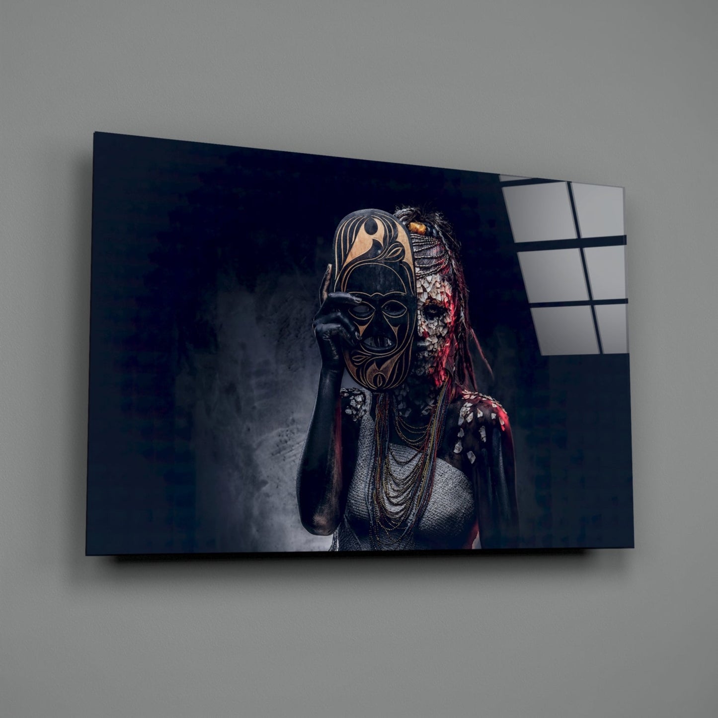Glass wall art mounted on gray wall showing masked figure in ornate gold and black mask with red fabric and beaded necklaces against dark background.