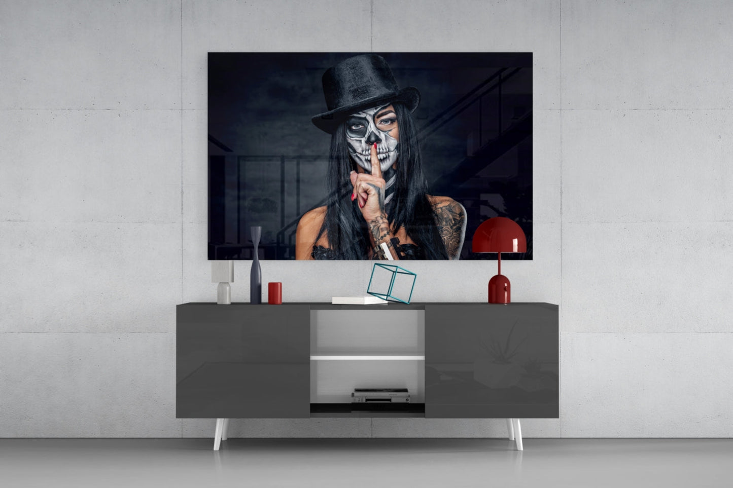 Modern media console with gray storage cabinet displaying glass wall art of woman with skull makeup and black hat above.