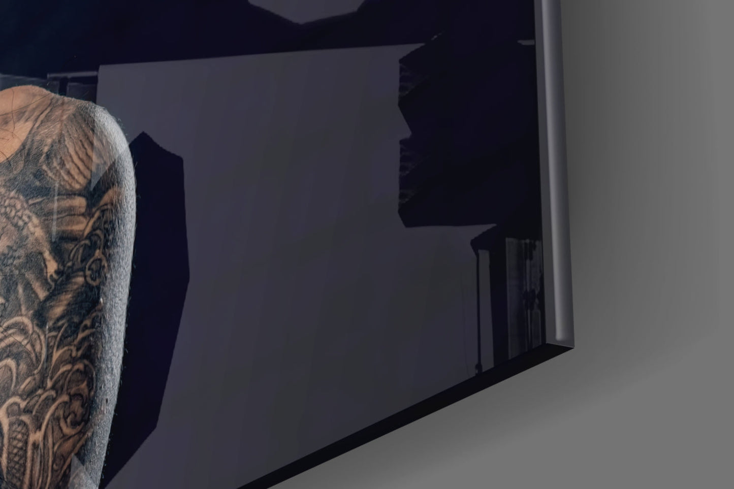Person with tattooed arm viewing dark frosted glass wall art panel mounted indoors.