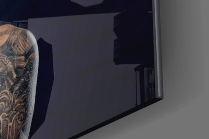 Person with tattooed arm viewing dark frosted glass wall art panel mounted indoors.