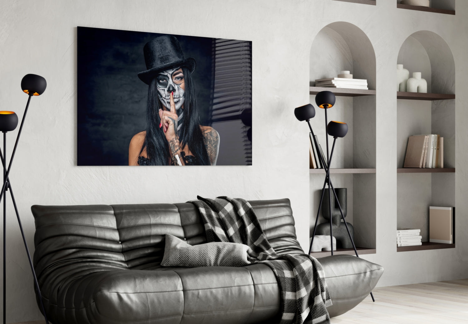 Glass wall art featuring a woman with skull face paint and black hat displayed above a gray leather sofa in modern interior setting.