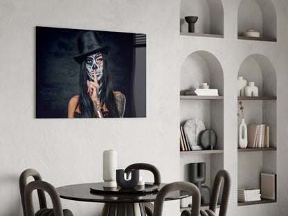 Skull-faced figure wearing black top hat with finger to lips, displayed as framed glass wall art above round black dining table.