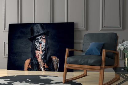 Glass wall art displaying skull-faced figure in black hat and long dark hair against dark background, mounted in modern living room setting.