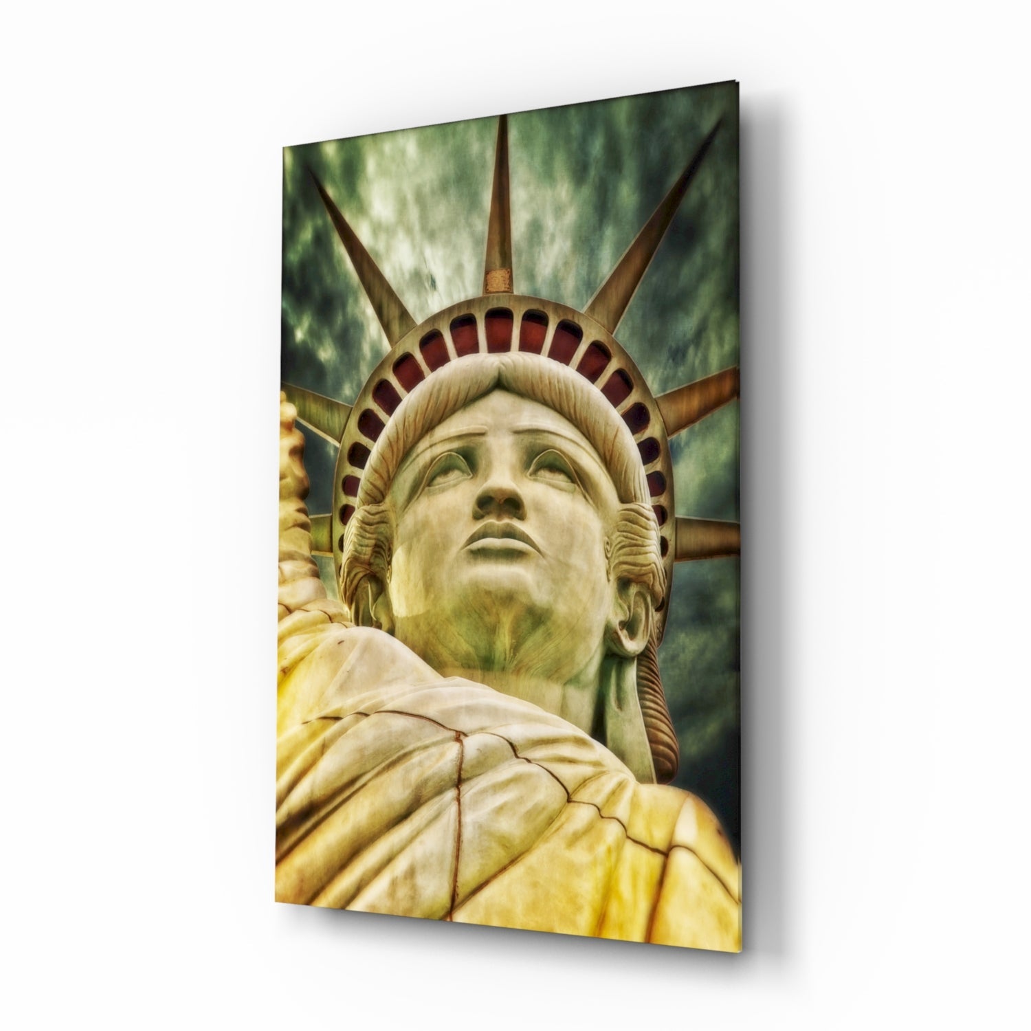 Close-up of Statue of Liberty's face and crown on glass wall art, viewed from below against green sky background.