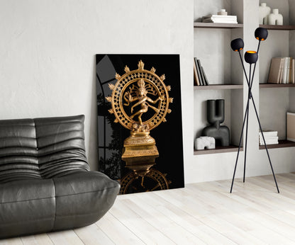 Golden Shiva Nataraja statue displayed on black glass panel in modern living room with gray sofa and shelving.