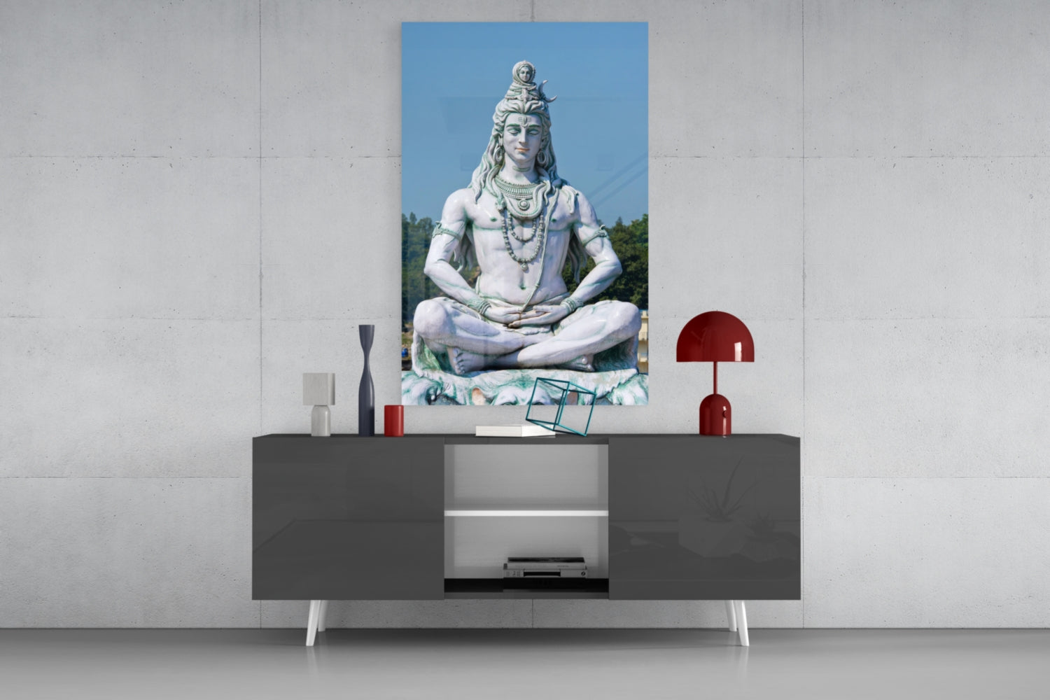 Glass wall art depicting a white stone Shiva statue in meditation pose displayed above a dark console table with decorative accessories.