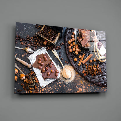 Glass wall art displaying chocolate bar with hazelnut toppings surrounded by coffee beans, cinnamon sticks, and cocoa powder on dark surface.