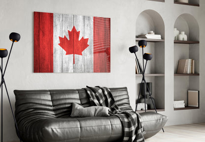 Canadian flag glass wall art displaying red and white maple leaf design hanging above black leather sofa in modern living room.