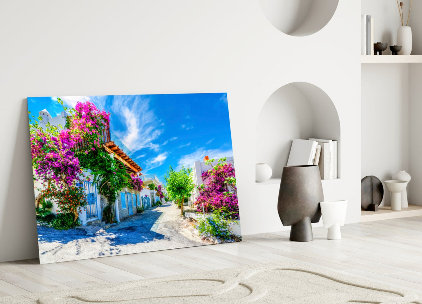 Glass wall art depicting a sunlit Mediterranean street with vibrant magenta bougainvillea flowers and whitewashed buildings, displayed in a minimalist room setting.