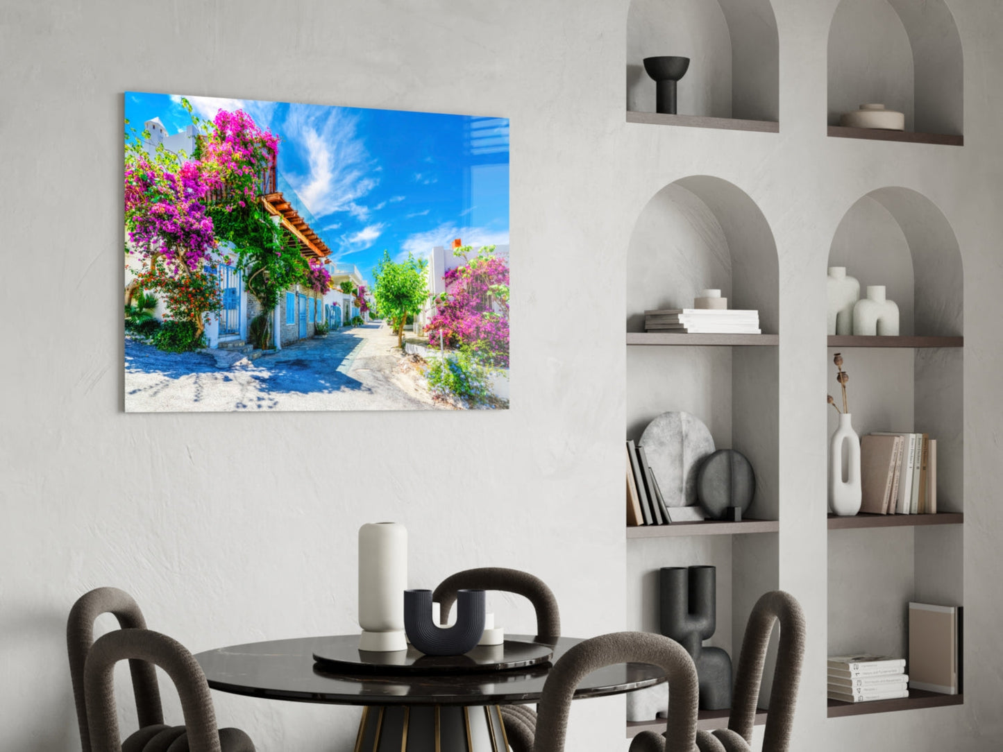 Colorful glass wall art depicting a Mediterranean street with magenta bougainvillea flowers and blue sky, displayed above a black dining table.