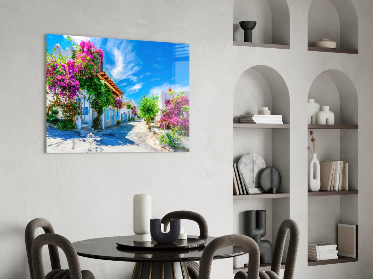 Colorful glass wall art depicting a Mediterranean street with magenta bougainvillea flowers and blue sky, displayed above a black dining table.