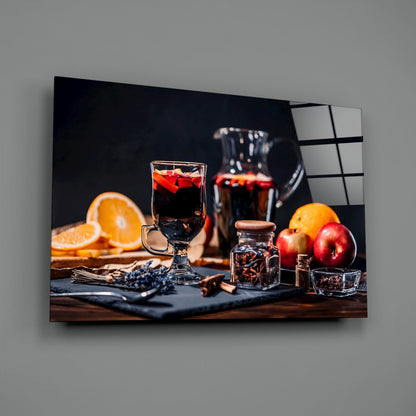 Noel Tea Glass Wall Art displayed on grey wall, featuring dark glass panel with festive holiday beverage setup including oranges, apples, spices, and dark liquid in glass.