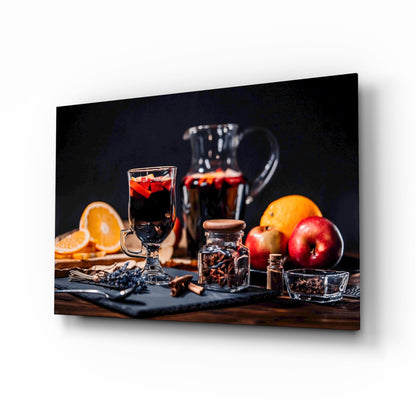 Festive holiday beverage display with mulled wine glass, fresh oranges, apples, spices, and decorative bottles on dark wooden surface against black background.