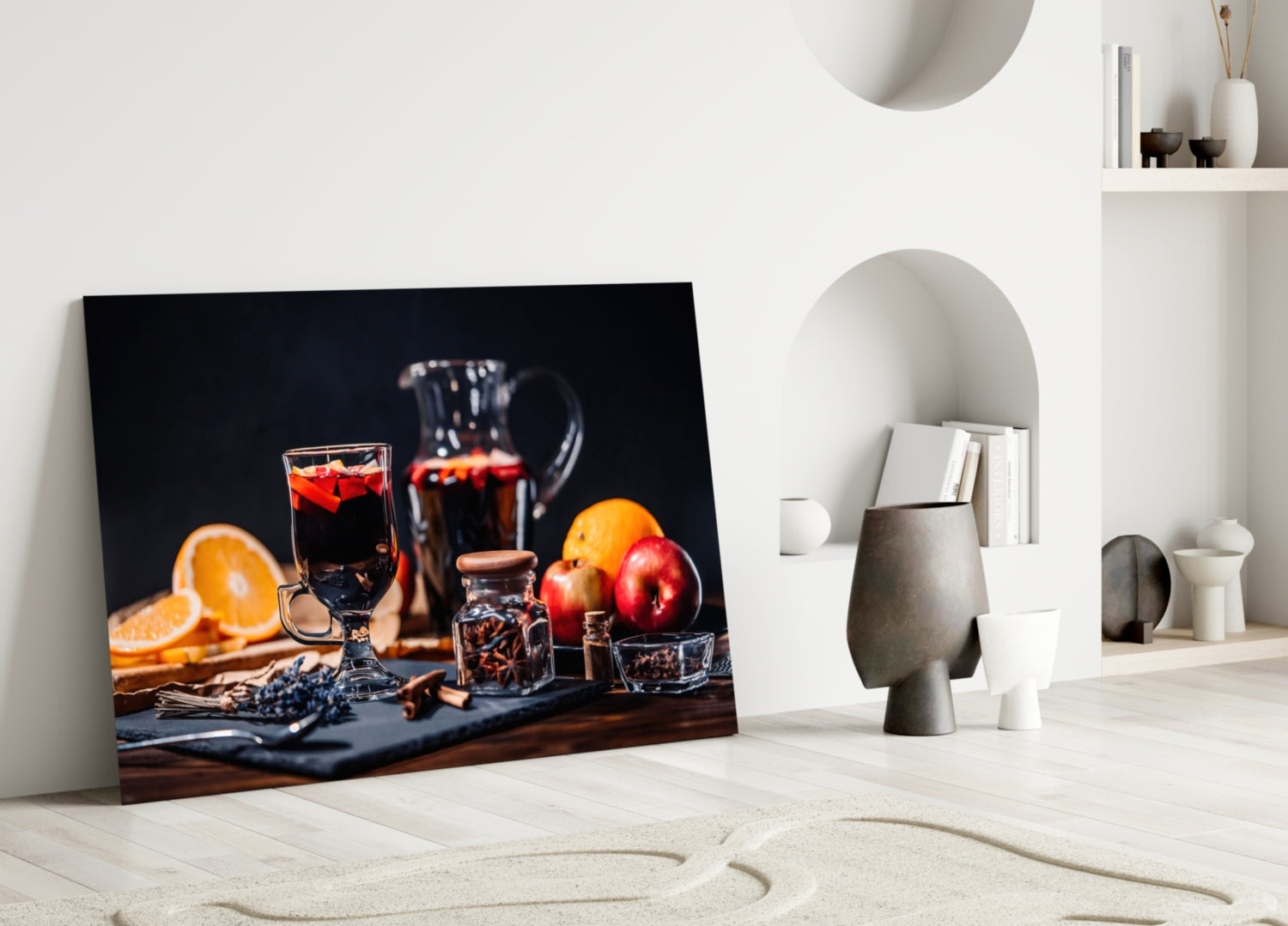 Noel Tea Glass Wall Art leaning against white wall displaying festive still life with dark beverages, citrus fruits, apples, and spices on dark surface.