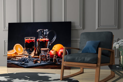 Black wall art displaying a festive holiday drink setup with red beverages, orange slices, apples, and glass bottles on dark surface.