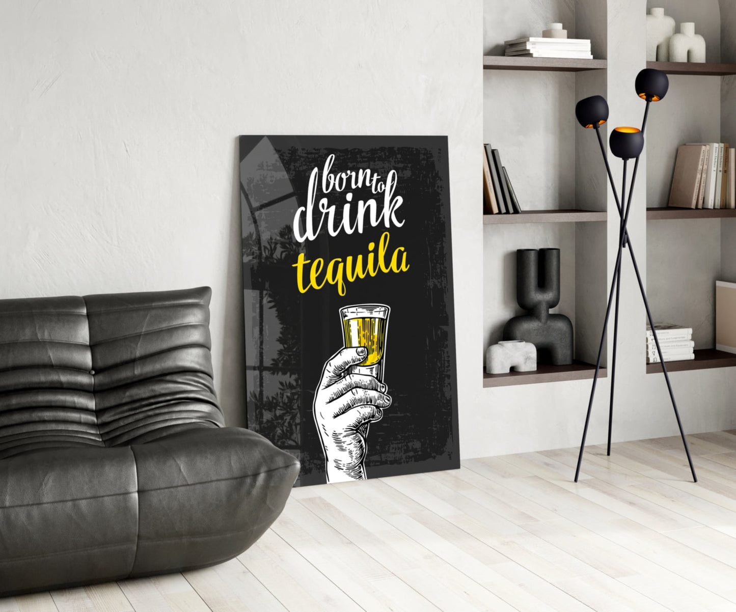 Black canvas wall art with "born to drink tequila" text in white and yellow, featuring a hand holding a tequila shot glass, leaning against white wall beside gray sofa in modern living room.