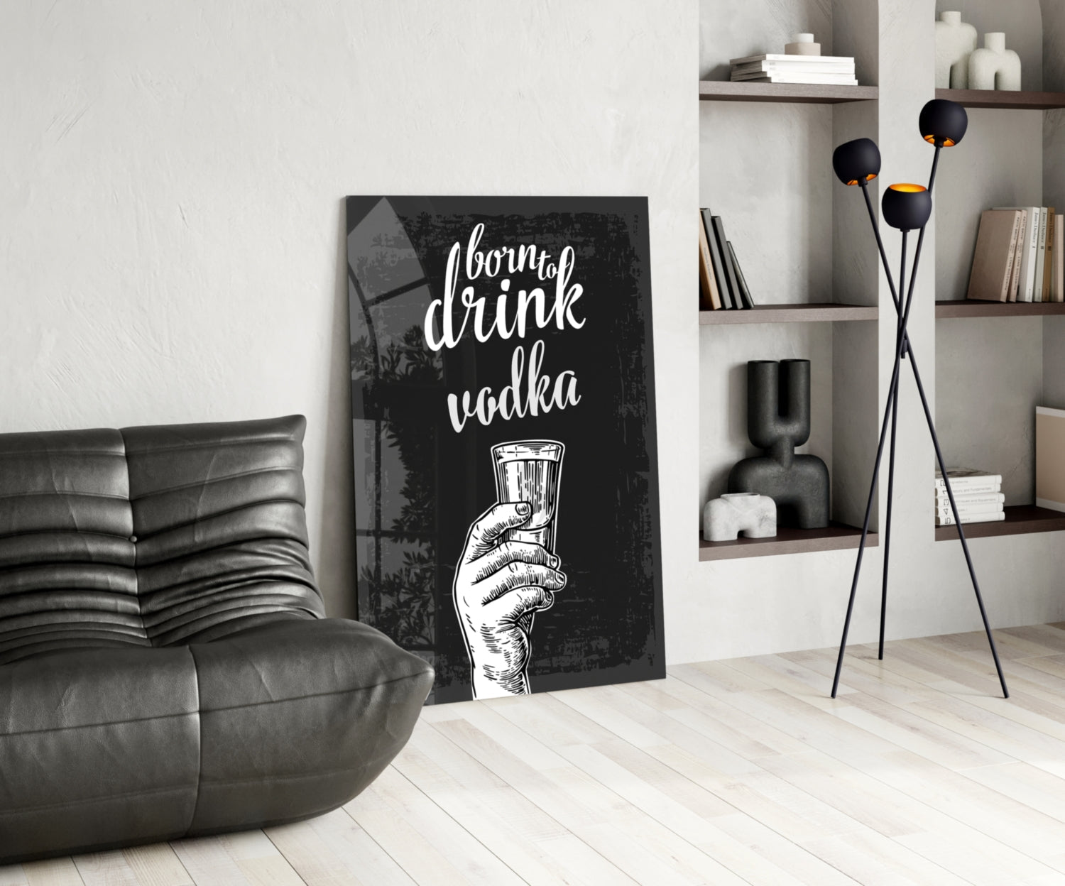 Black canvas wall art with white script text "born to drink vodka" and hand holding glass, displayed in modern living room with gray sofa and wooden shelving.
