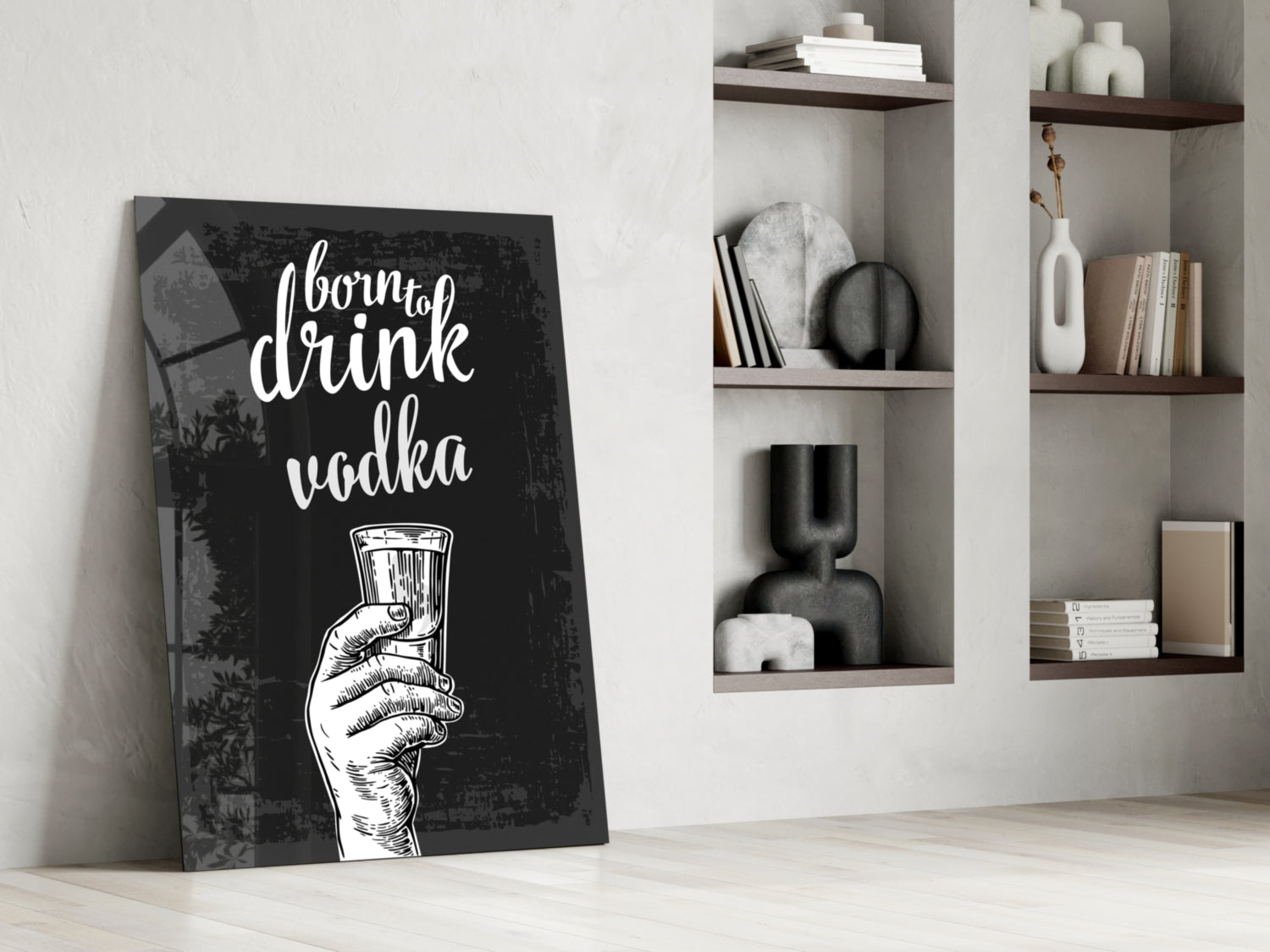 Black canvas wall art with white text reading "about to drink vodka" and hand holding glass, leaning against white wall beside wooden shelving.