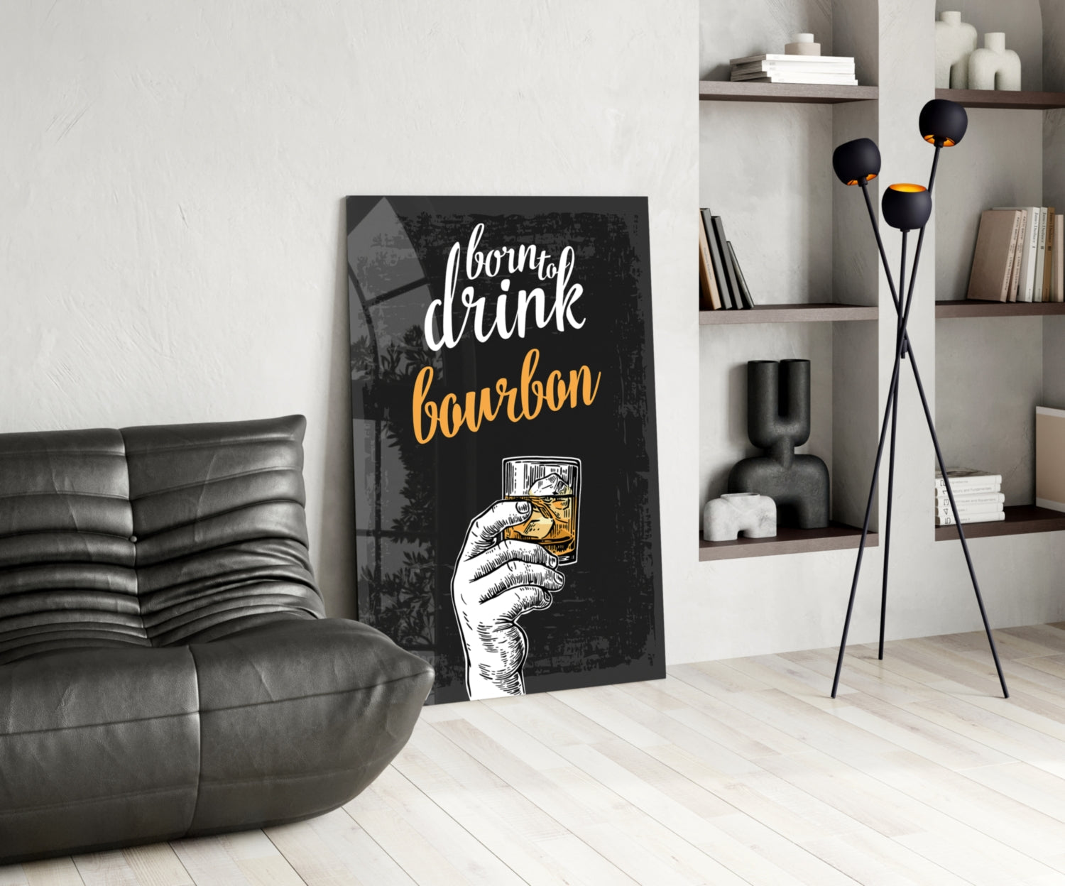 Black canvas wall art with "born to drink bourbon" text in white and gold lettering, leaning against white wall beside gray leather chair and styled shelving unit.