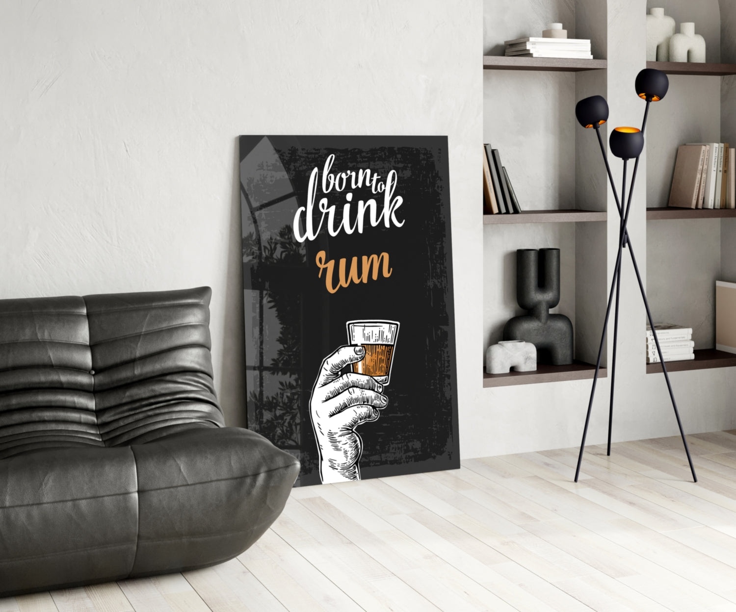 Black canvas rum wall art with white and gold text and hand illustration leaning against white wall beside gray leather chair.