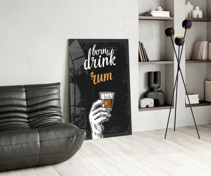 Black canvas rum wall art with white and gold text and hand illustration leaning against white wall beside gray leather chair.